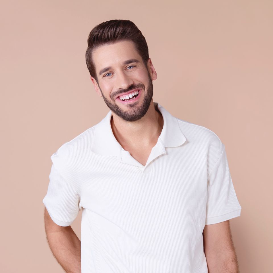 mann-mit-dunklem-haar-und-bart-trägt-weißes-polohemd-und-lächelt-vor-beigem-hintergrund