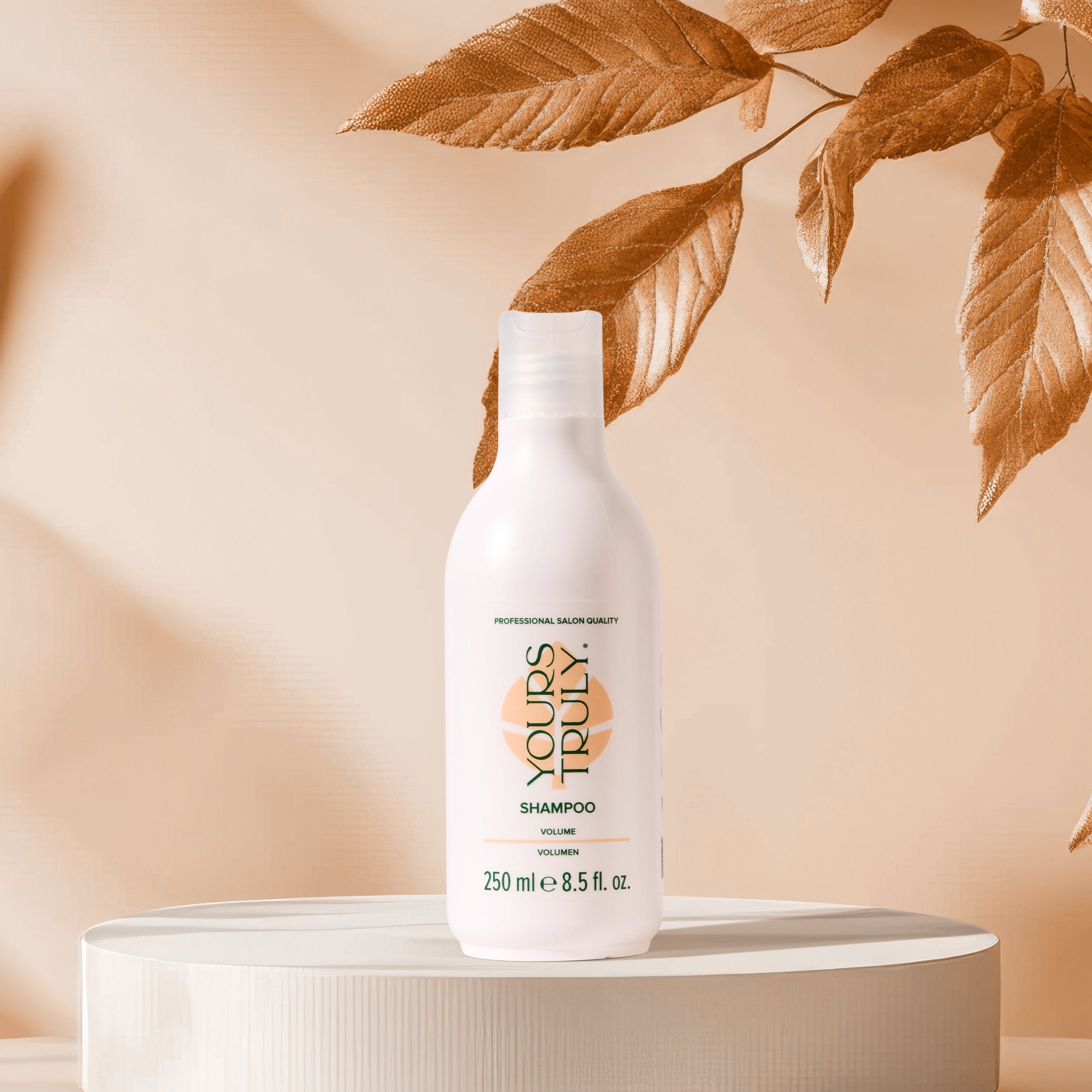 yours-truly-volumen-shampoo-in-weißer-250ml-flasche-auf-rundem-podest-mit-beigen-hintergrund-und-dekorativen-blättern