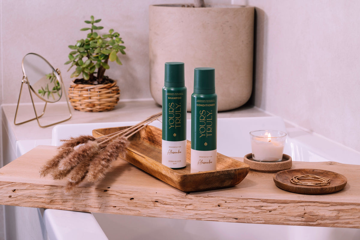 zwei-grüne-flaschen-shampoo-und-conditioner-auf-holzablage-neben-kerze-getrockneten-gräsern-und-schmuckschale-im-badezimmer