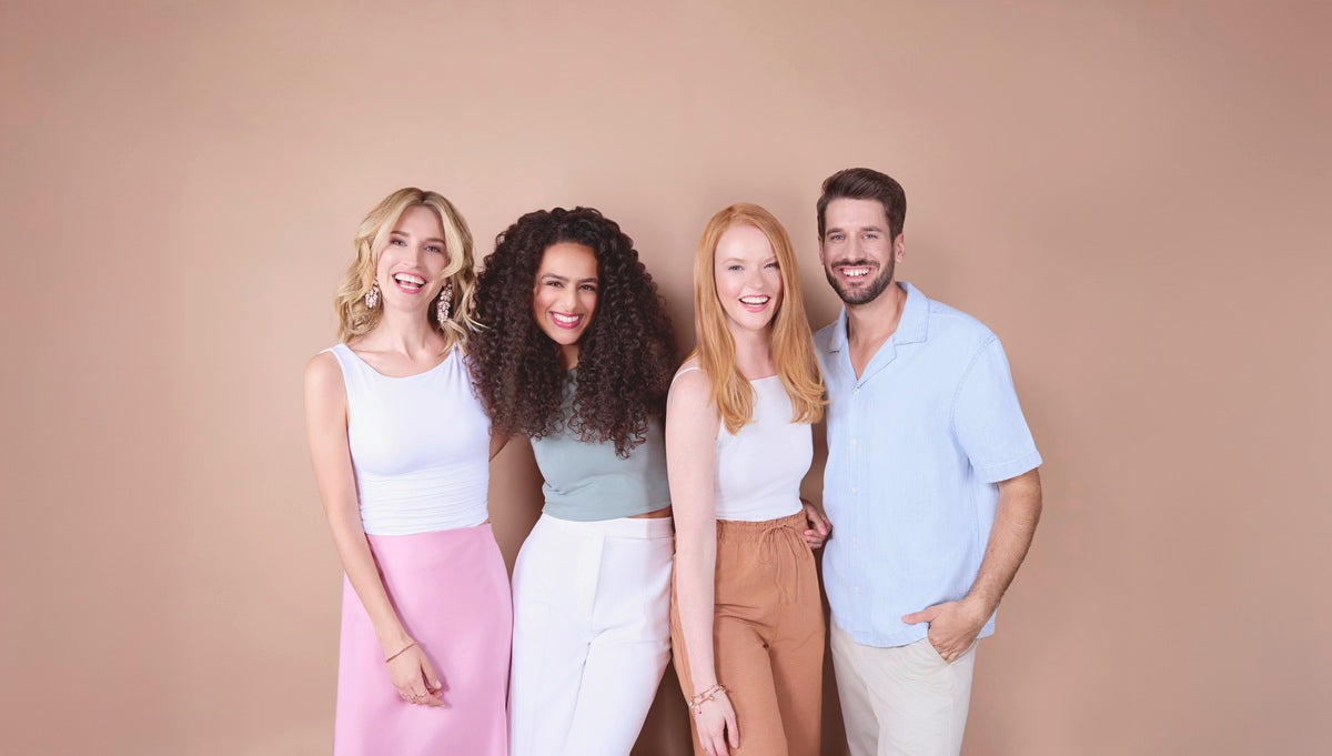 vier-lachende-personen-zwei-frauen-mit-lockigem-und-glattem-haar-eine-frau-mit-roten-haaren-und-ein-mann-mit-bart-stehen-nebeneinander-lächelnd-vor-beigem-hintergrund